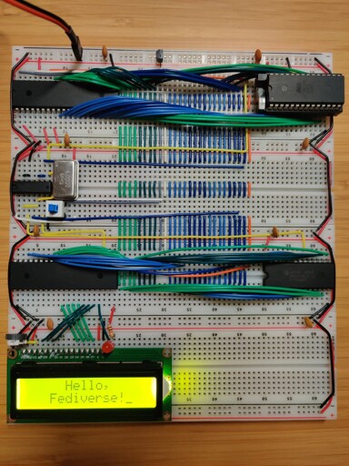 A set of breadboards with a 65c02 microprocessor and associated components. An LCD screen on one of the boards reads "Hello, Fediverse!"